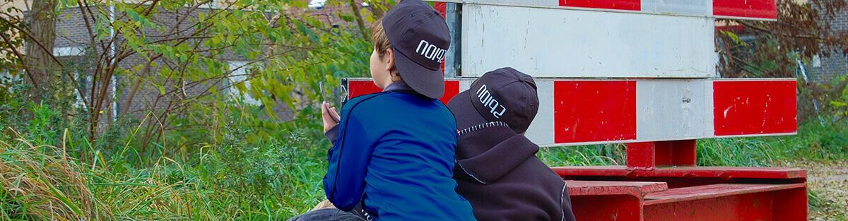 Twee jongens van 8 en 9 jaar zijn buiten bezig met een speurtocht en zoeken naar een aanwijzing.