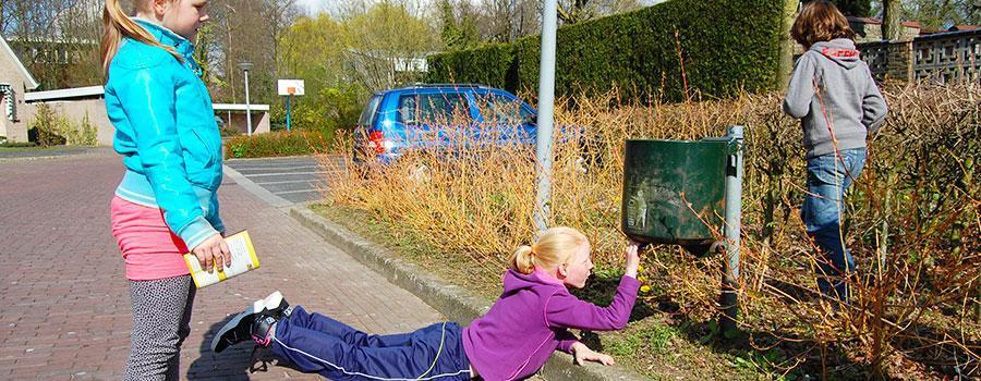 Een meisje dat onder een prullenbak op zoek is naar de verstopte envelop